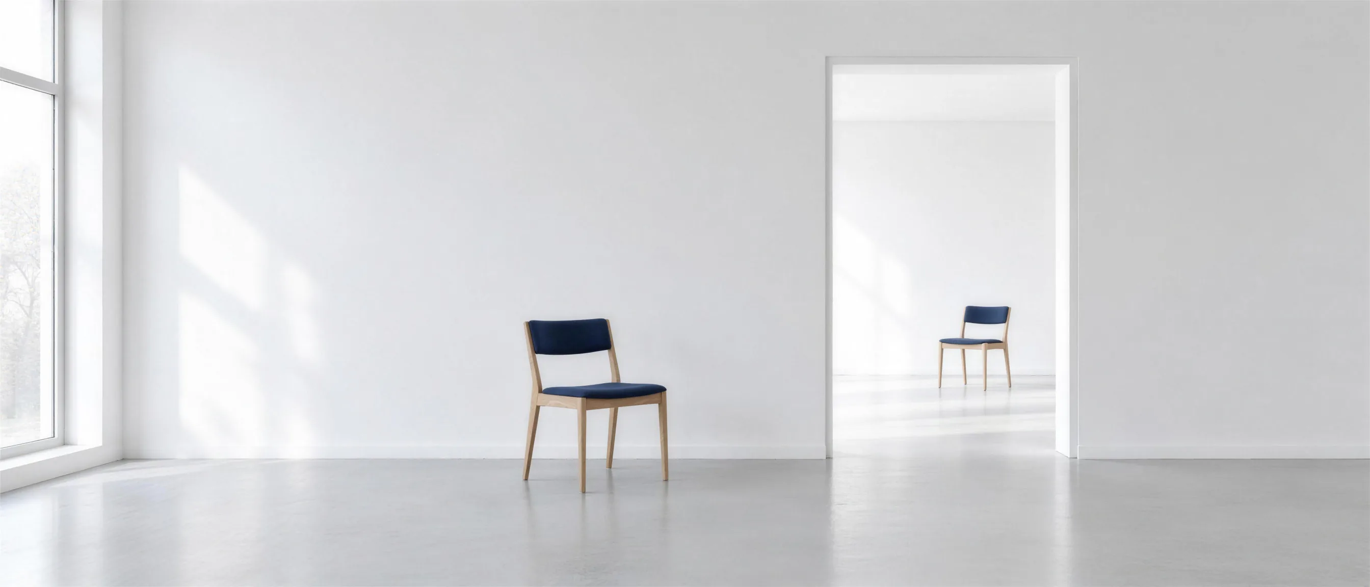 A chair with dark blue upholstery in a bright room; through an open door, the same chair stands in the next room