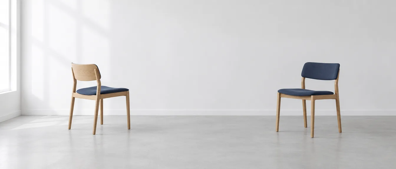 Two chairs with dark blue upholstery stand apart in a bright room, one turned slightly away