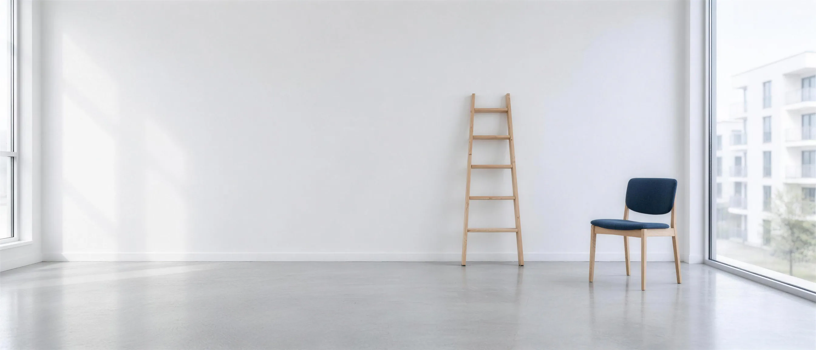 A wooden ladder and a chair with dark blue upholstery in an empty, bright room, with a view through the window of a new building