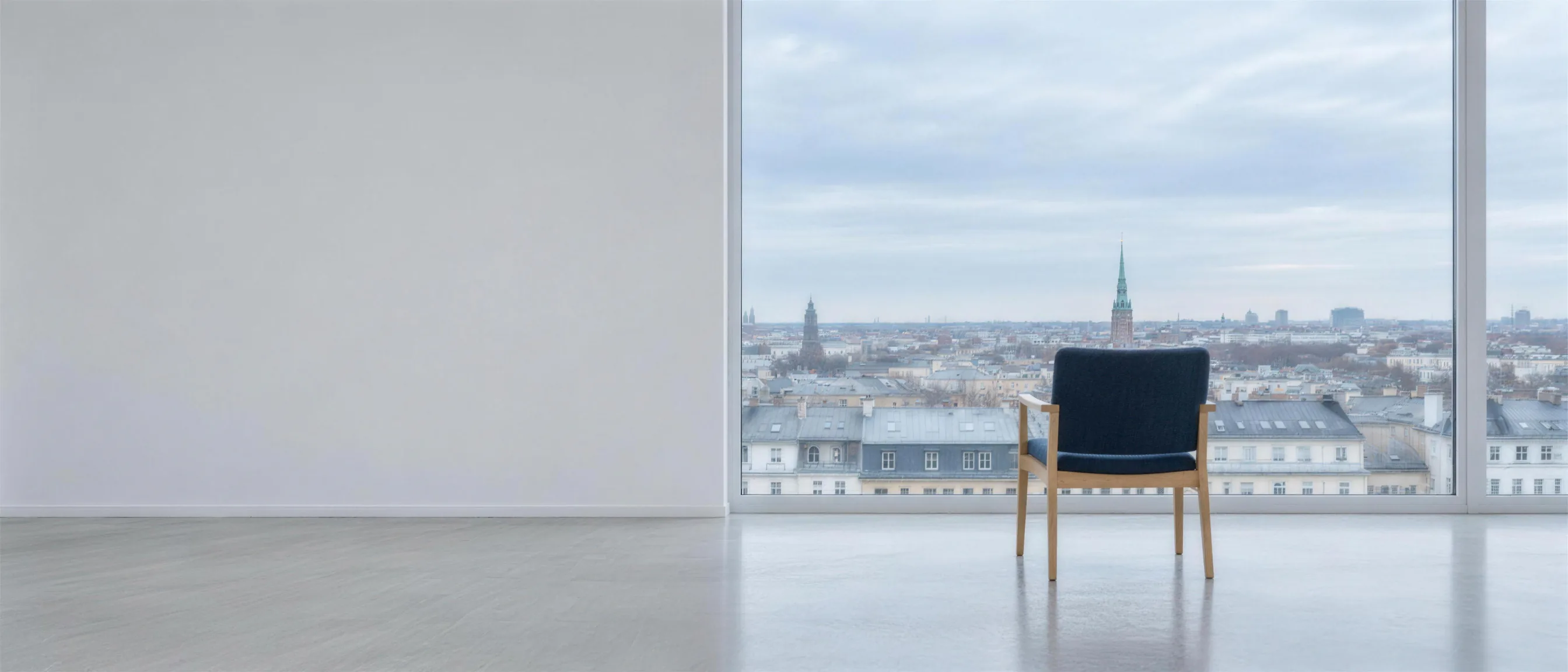 An armchair with dark blue upholstery in front of a floor-to-ceiling window front overlooking the rooftops of the city